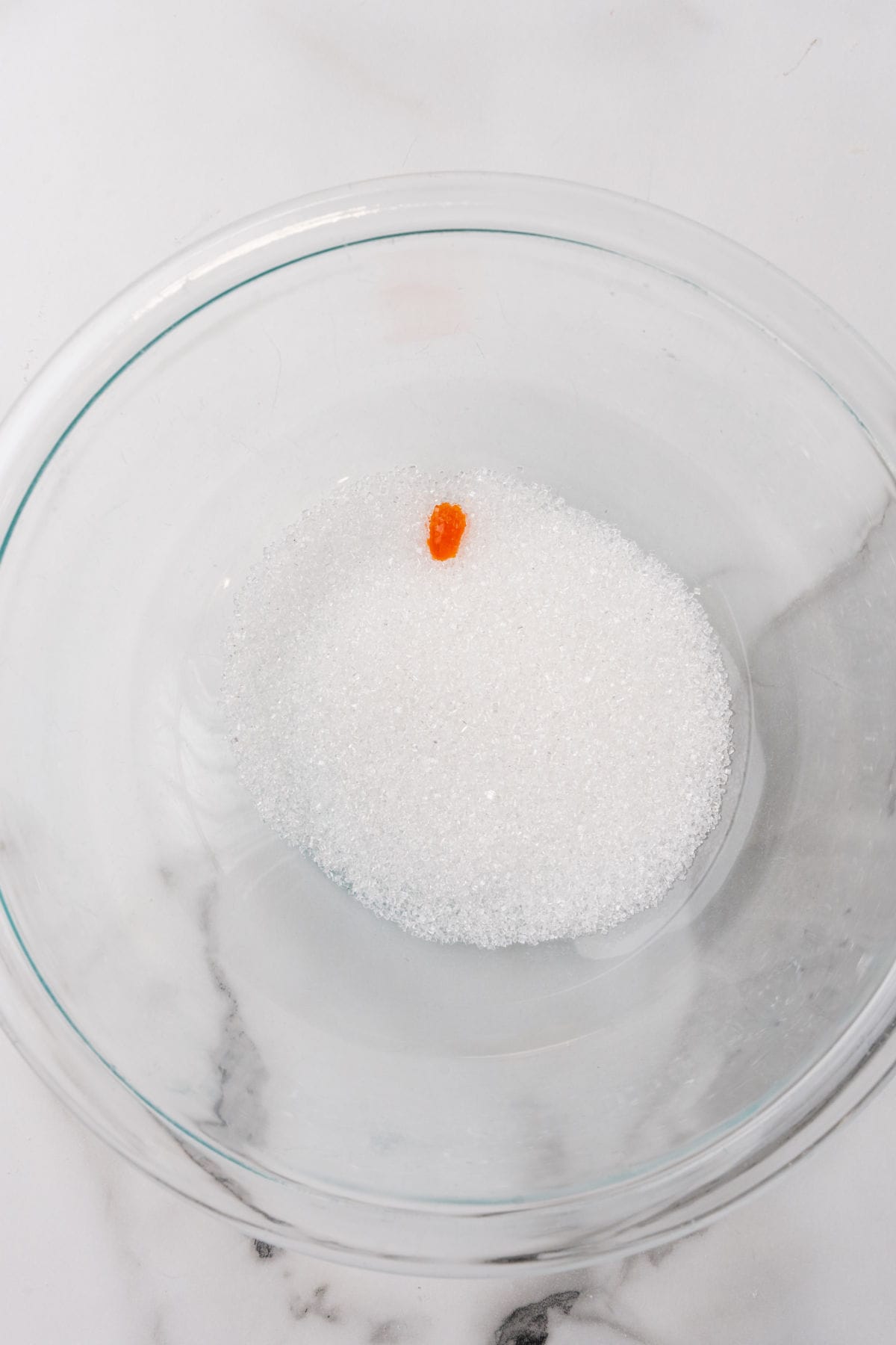 Yellow food color in white sanding sugar in a clear glass bowl.