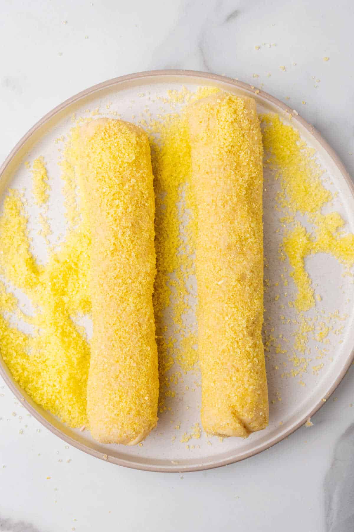 Two cookie dough logs rolled in yellow sugar on a plate.