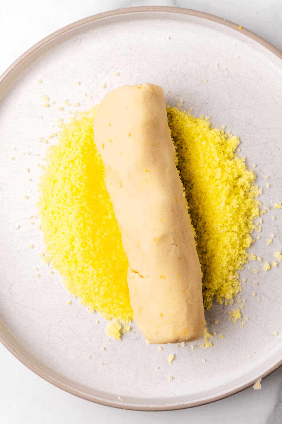A shortbread cookie dough log in yellow sugar on a white plate.