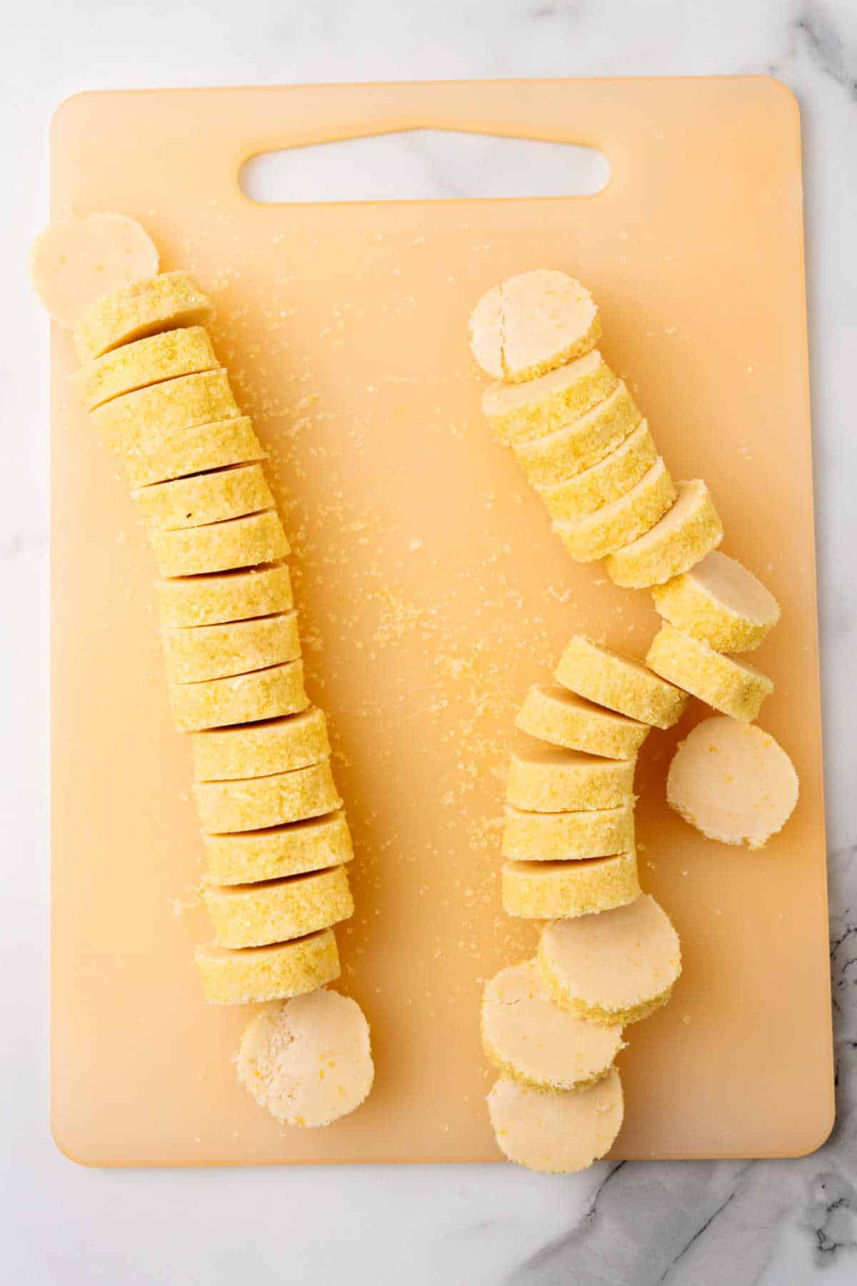 Slices of lemon shortbread cookie dough on a cutting board.
