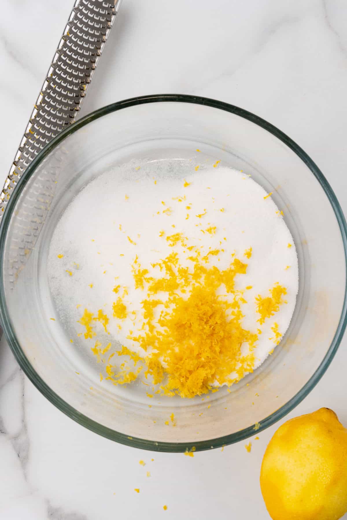 Sugar and lemon zest in a glass bowl.