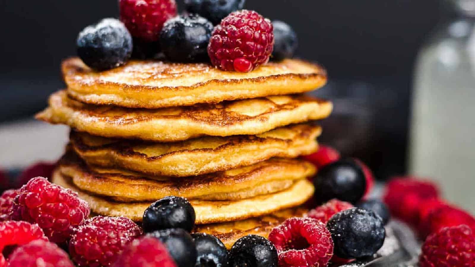 A stack of pancakes topped with blueberries and raspberries, with additional berries scattered around the base.