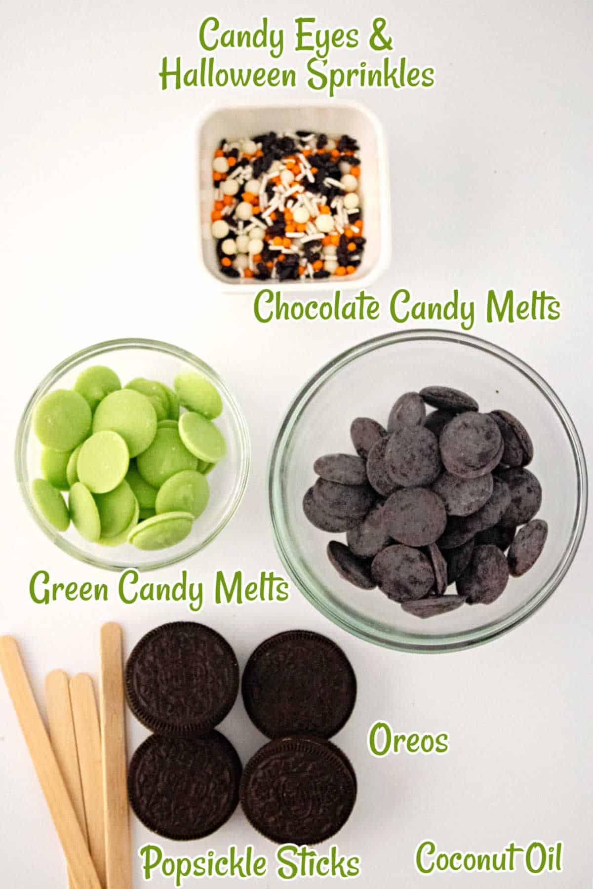 Halloween Oreo cauldron pops with candy eyes, Halloween sprinkles, green and chocolate candy melts, Oreos, popsicle sticks, and coconut oil placed on a white surface.