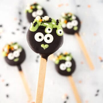 Four Halloween-themed chocolate popsicles, decorated to look like monsters with googly eyes and green icing on wooden sticks, resembling delightful cauldron pops.