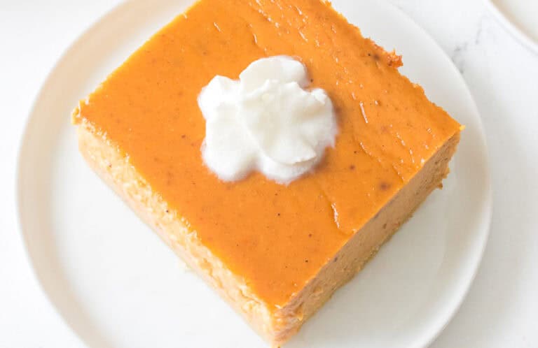 A slice of pumpkin pie topped with a dollop of whipped cream on a white plate.