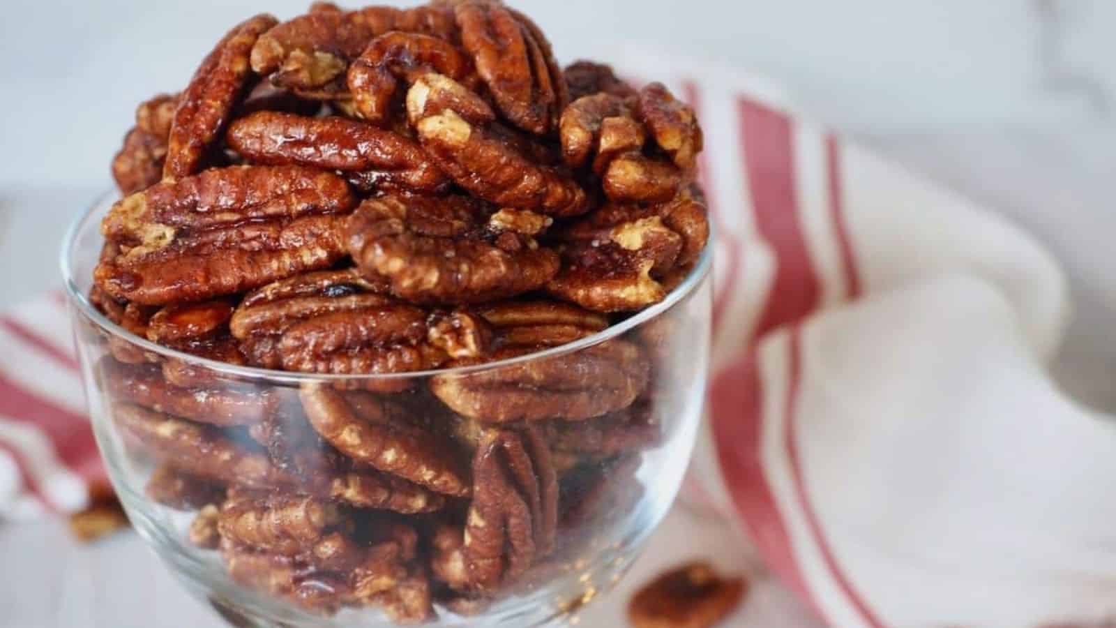 A glass bowl filled with pecans sits on a countertop next to a white and red striped cloth.