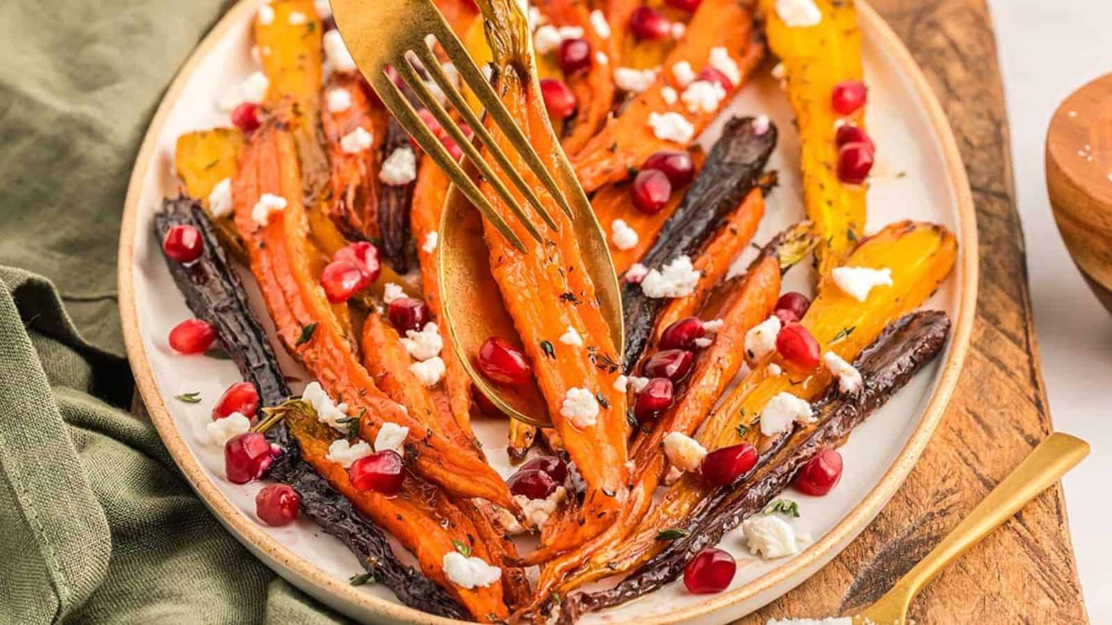 A plate of roasted carrots topped with crumbled cheese and pomegranate seeds, with a fork holding one carrot slice.