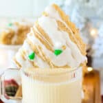 A frosted triangle-shaped scone topped with holiday-themed decorations rests on the rim of a glass cup filled with a creamy beverage.