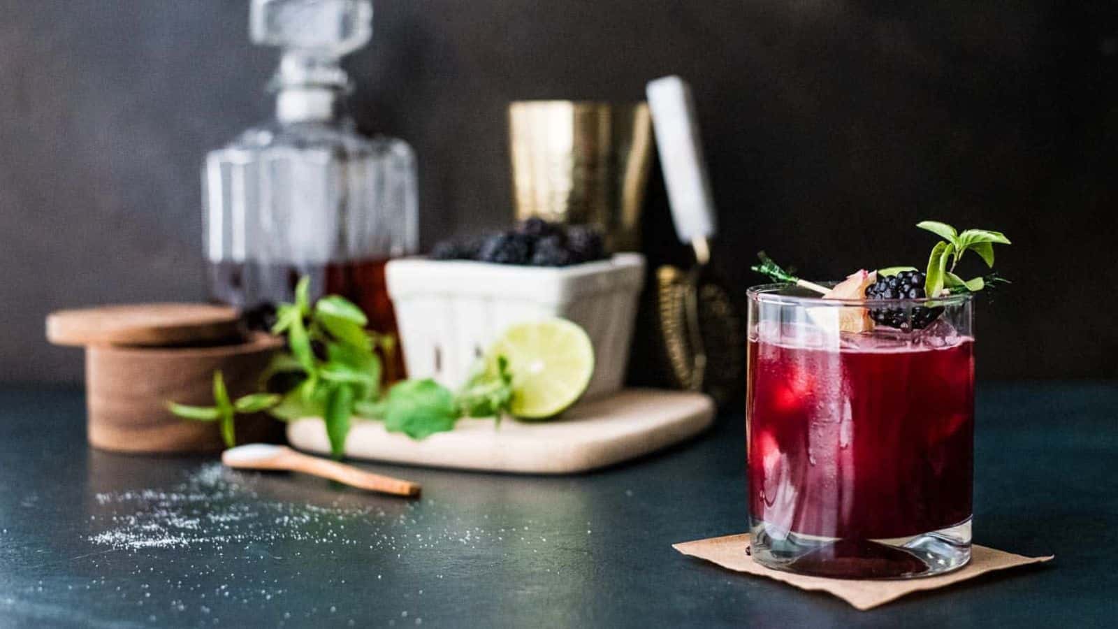 A blackberry bourbon smash in front of a cocktail bar set up.