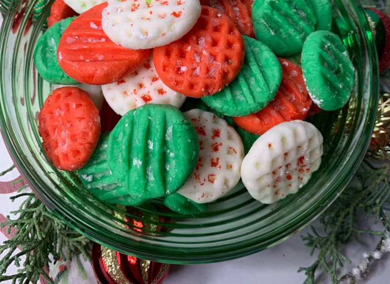 A green bowl filled with red, white, and green cookies shaped with a grid pattern, sprinkled with red sugar.
