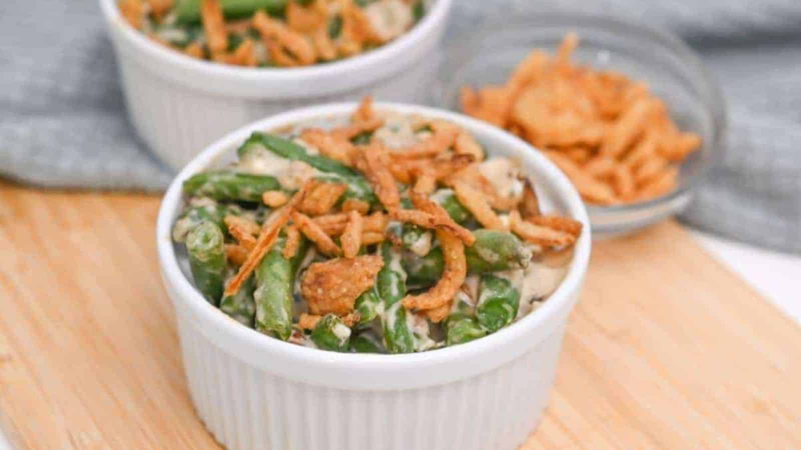 Two bowls of green bean casserole on a cutting board.