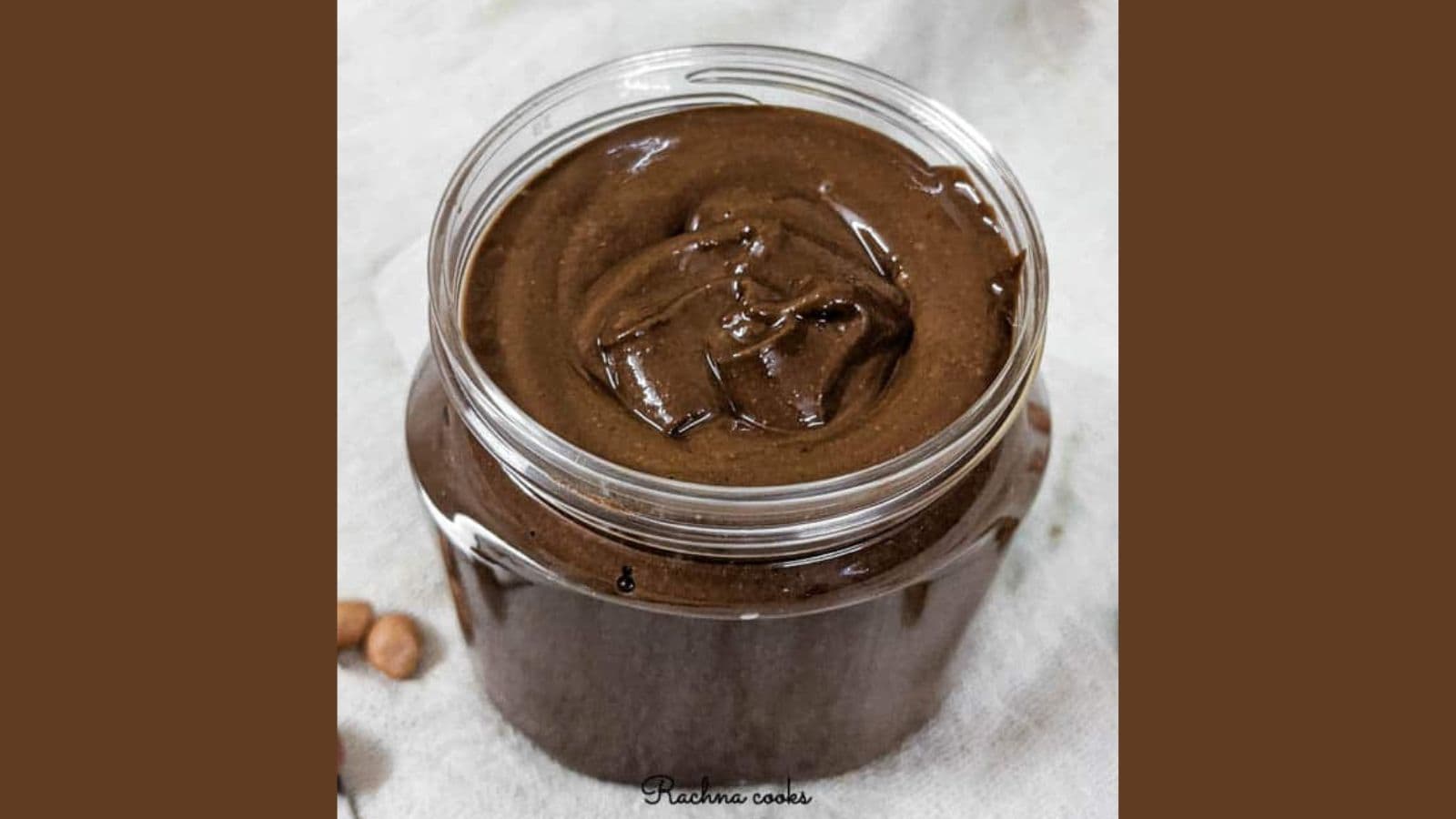 A jar filled with creamy, dark brown chocolate spread on a light cloth surface.