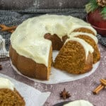 A spiced bundt cake with white icing is sliced on a plate. Nearby are star anise and cinnamon sticks.