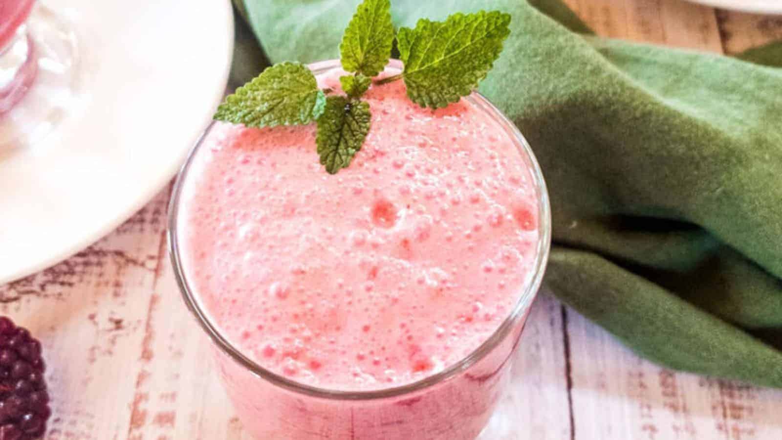 Blackberry smoothie in glass with mint garnish on white wood.