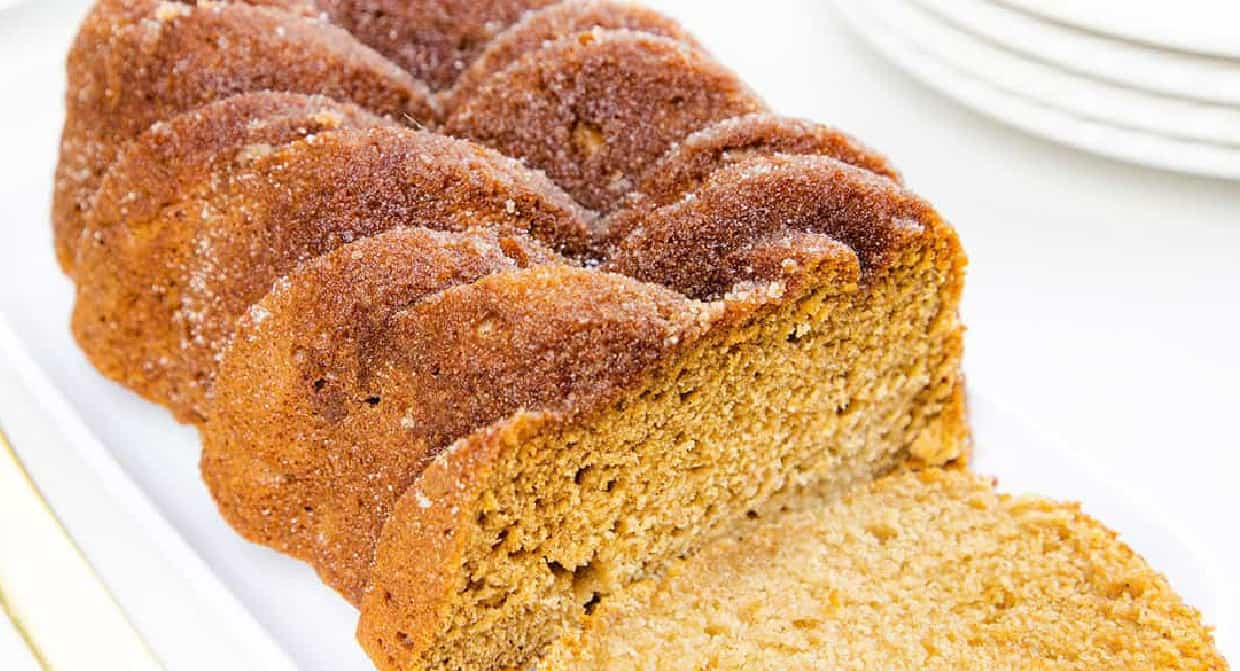 Sliced cinnamon sugar bread on a white tray, revealing a soft interior, with stacked white plates in the background.
