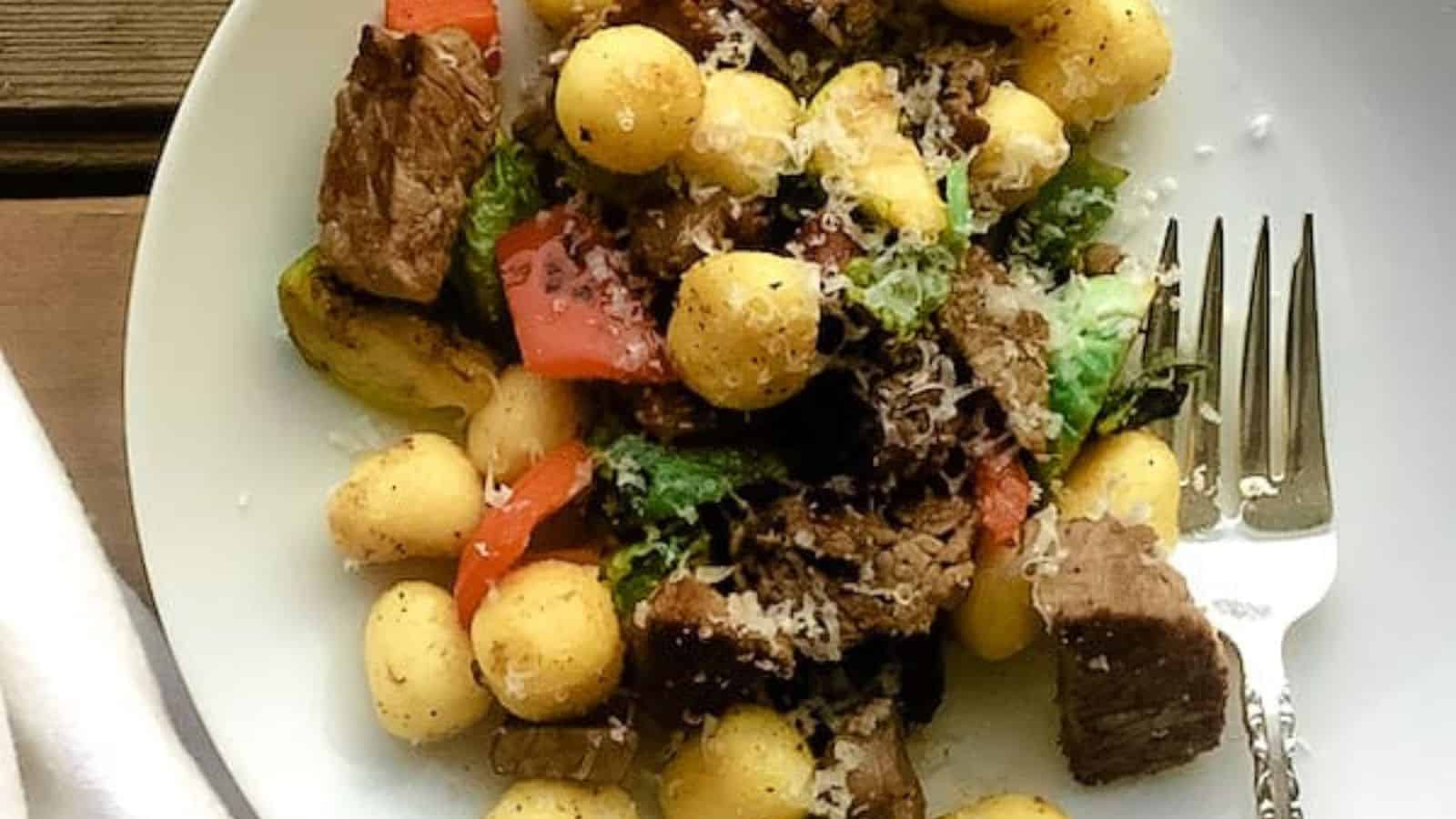 Leftover prime rib, gnocchi, and vegetables on a plate.