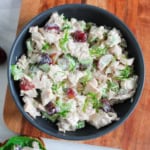 A bowl of chicken salad with grapes, celery, and dill on a wooden surface.