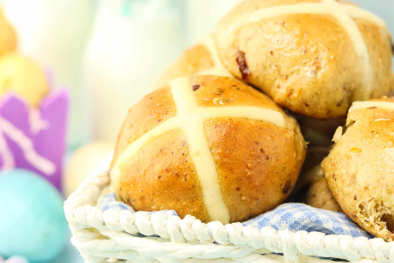 A basket of freshly baked hot cross buns with white icing crosses, placed on a blue and white cloth.