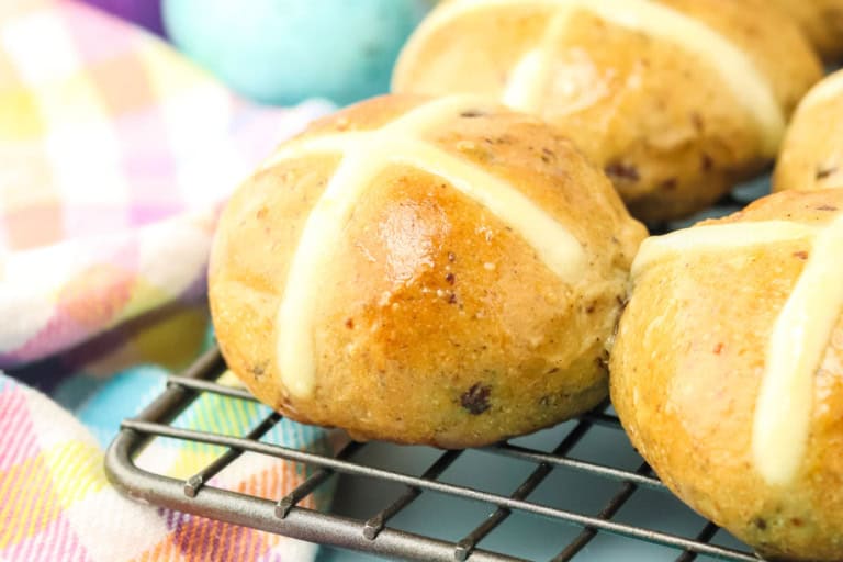 Close-up of hot cross buns on a cooling rack, with a plaid cloth in the background.