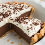 Chocolate cream pie with a slice missing, topped with whipped cream and chocolate shavings in a pie dish.