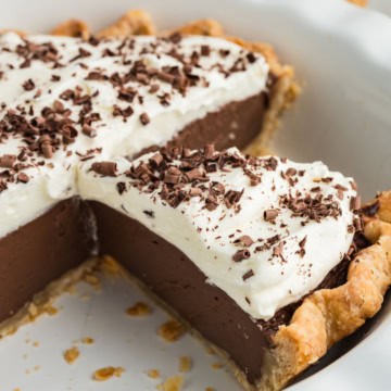 Chocolate cream pie with a slice missing, topped with whipped cream and chocolate shavings in a pie dish.