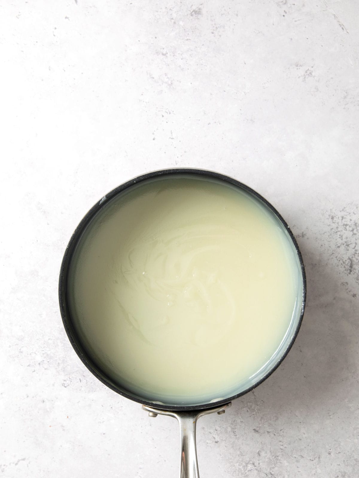 A saucepan containing a smooth, pale green liquid sits on a light gray surface.