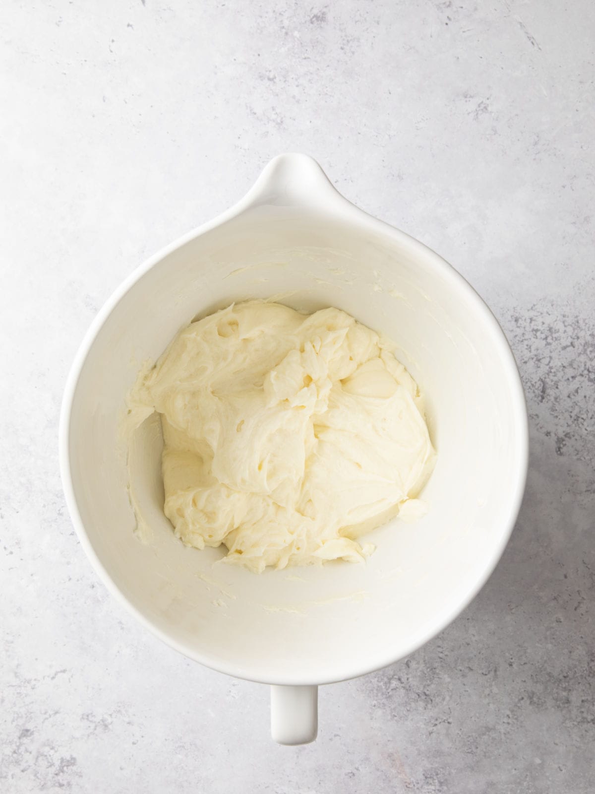 White ceramic bowl containing smooth, creamy white batter, placed on a light gray textured surface.
