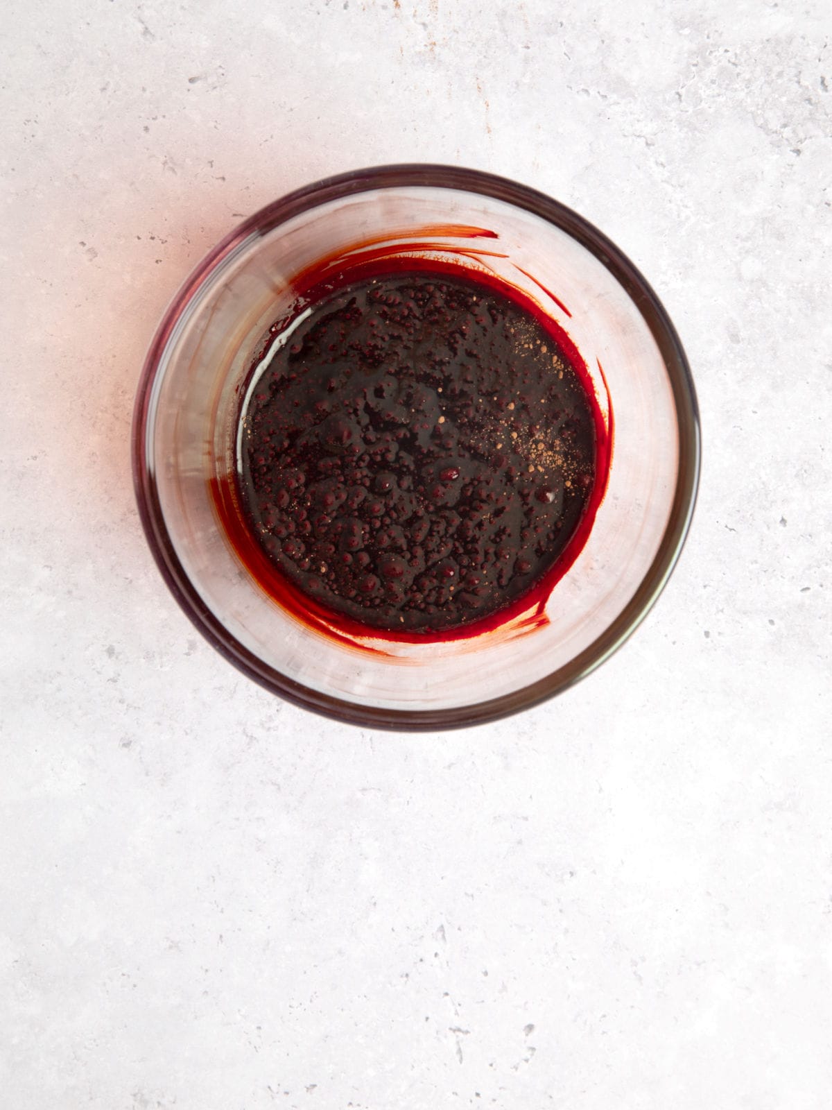 A glass bowl containing a thick, dark reddish-brown substance sits on a light gray surface.