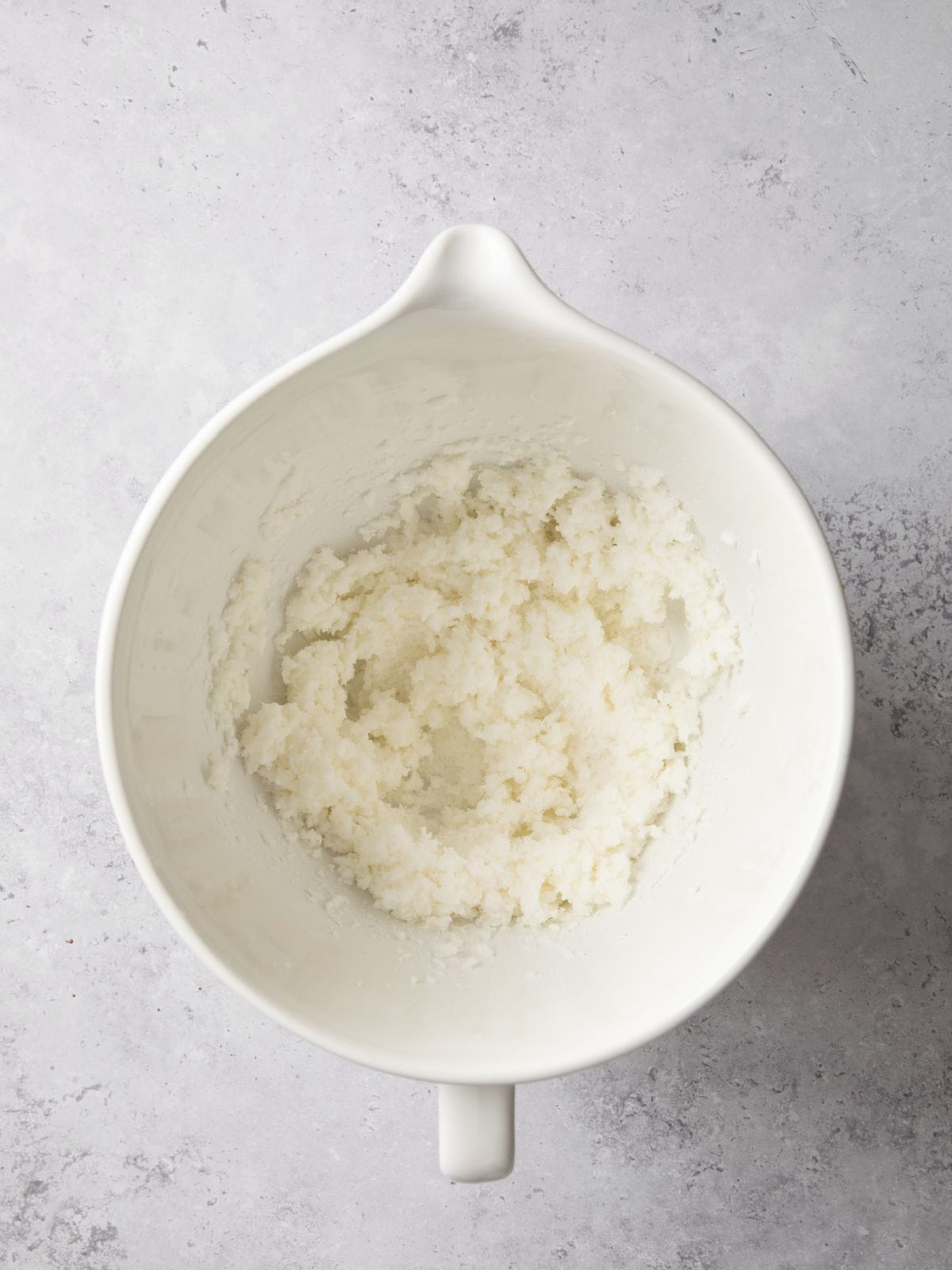 White ceramic mixing bowl containing a white, crumbly mixture on a light gray marbled surface.
