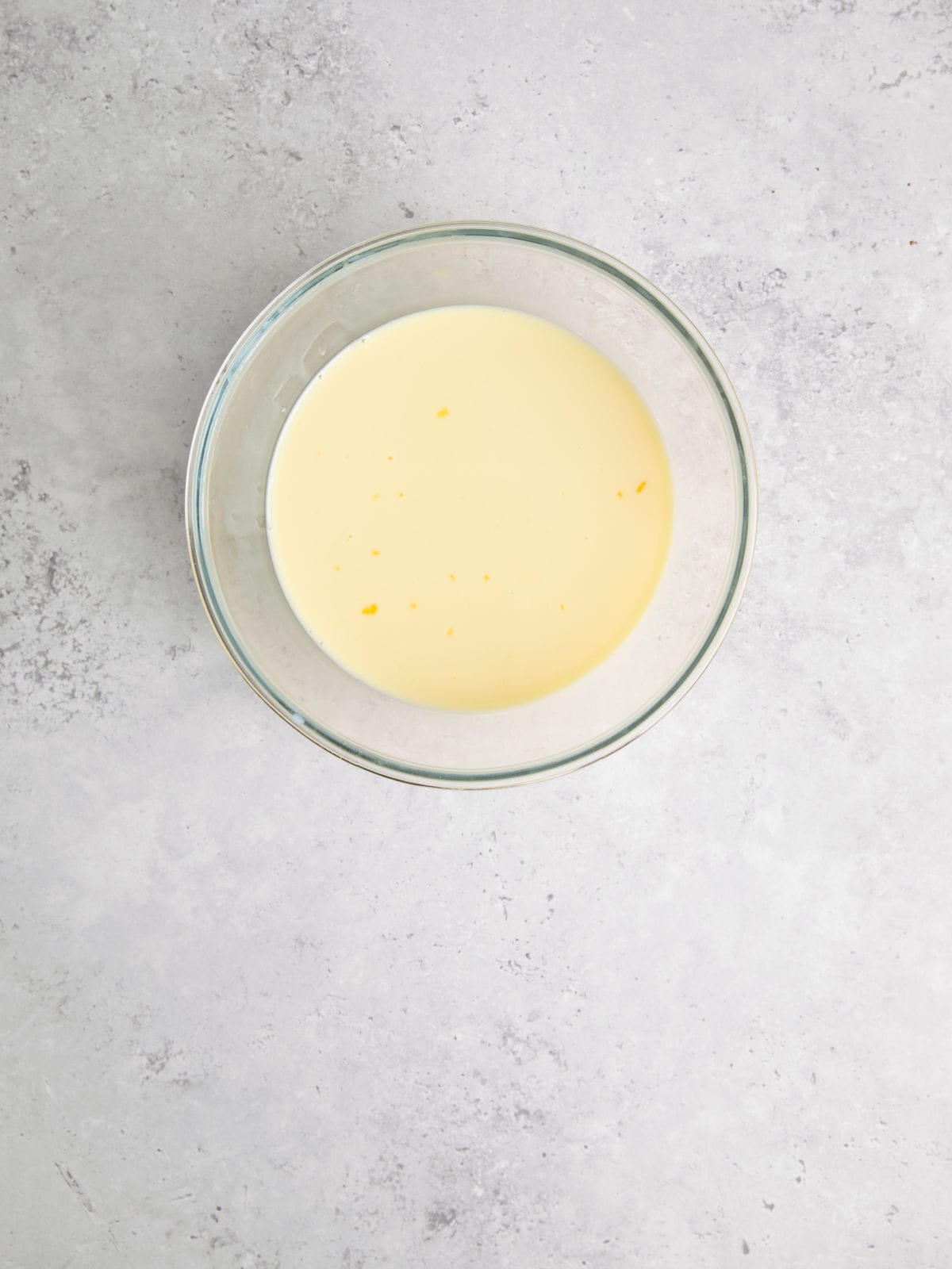 A glass bowl filled with a creamy yellow liquid sits on a gray, speckled surface.