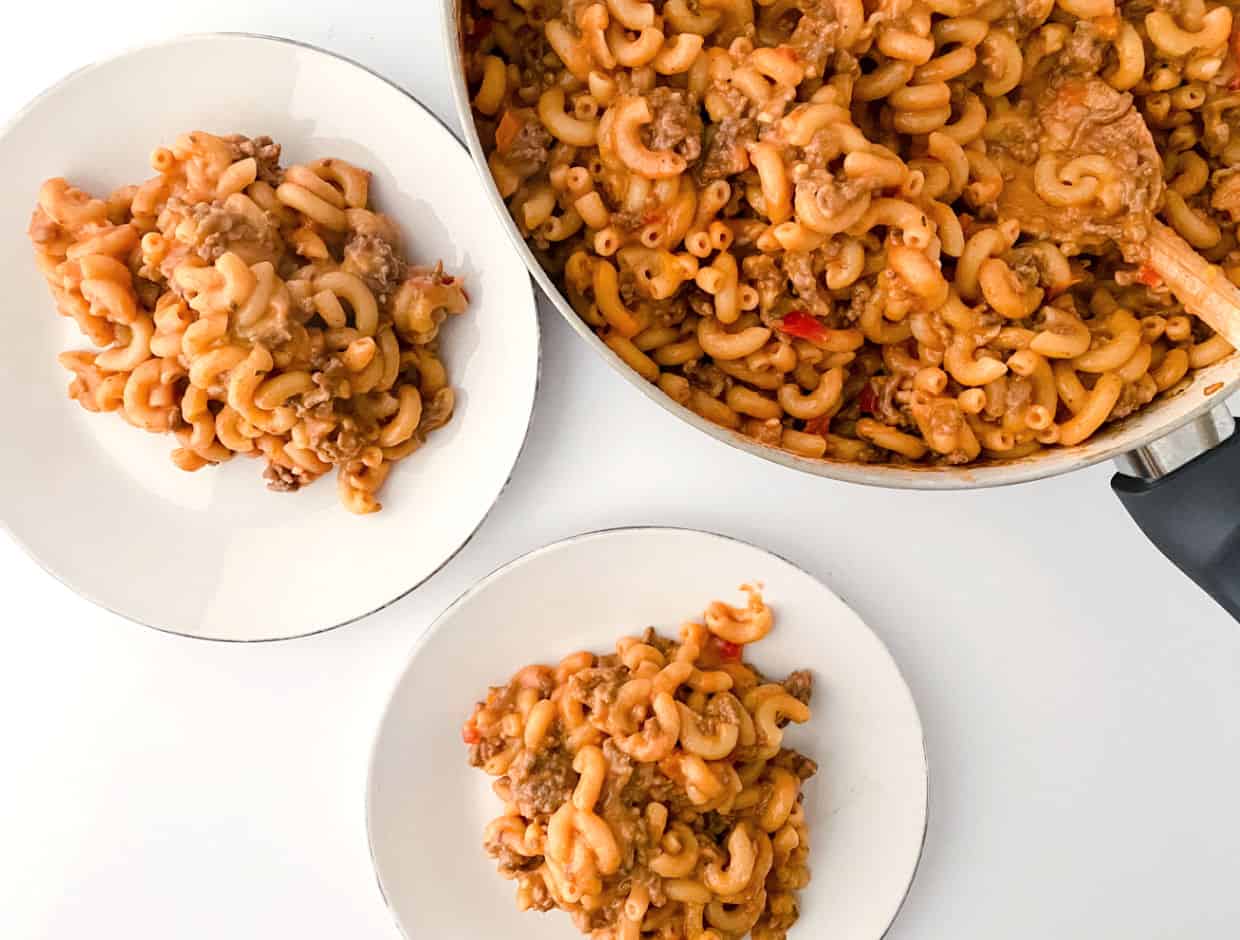 A pot of cooked macaroni with ground meat and sauce, with two servings plated on white dishes next to it.