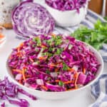 A white bowl filled with a colorful salad of shredded purple cabbage, carrots, and green herbs. Additional chopped cabbage and herbs are in the background.
