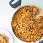 A pot filled with cooked macaroni pasta mixed with ground meat and cheese. A portion is served on a nearby white plate.