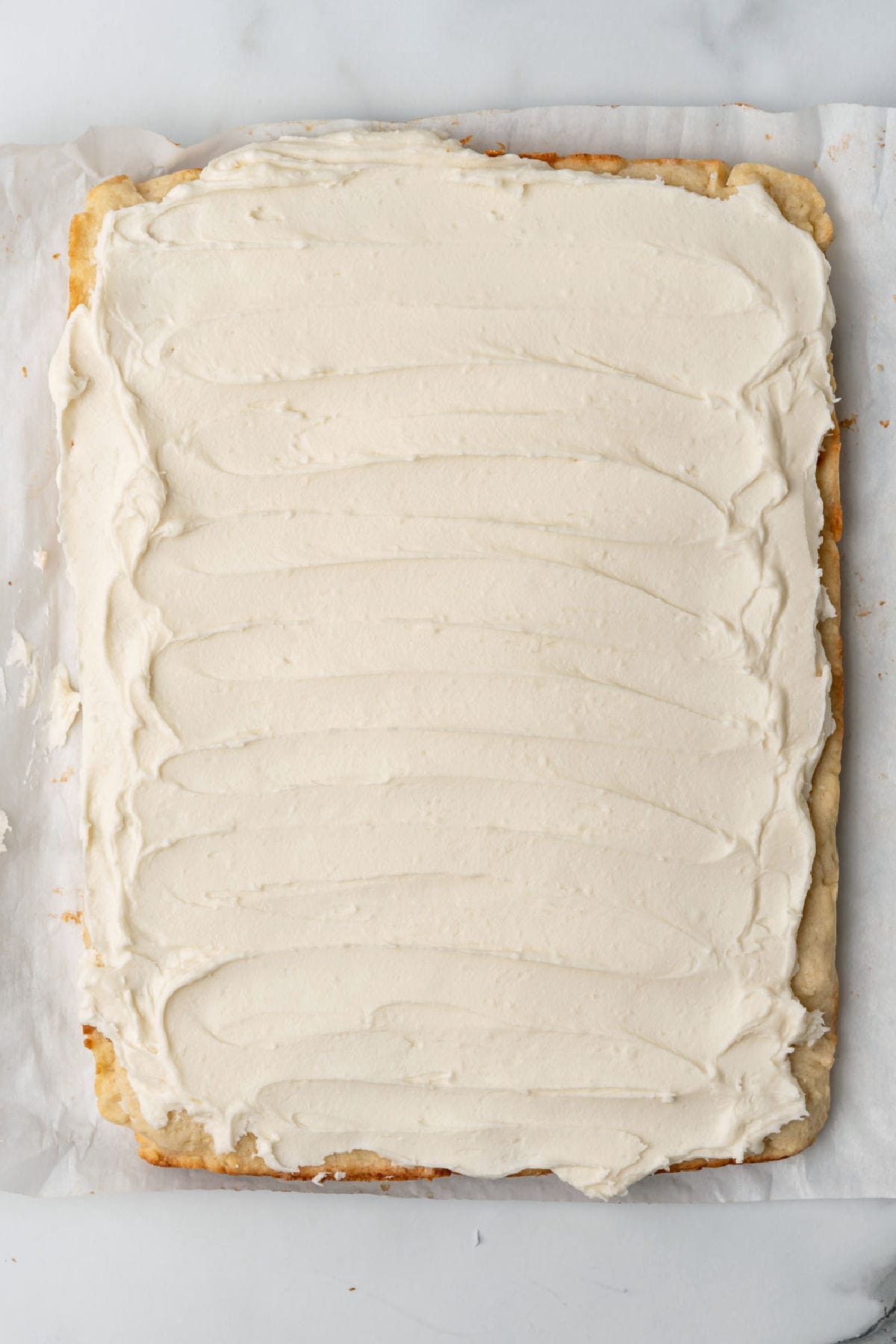 A rectangular sheet cake with smooth, white frosting on top, placed on parchment paper.