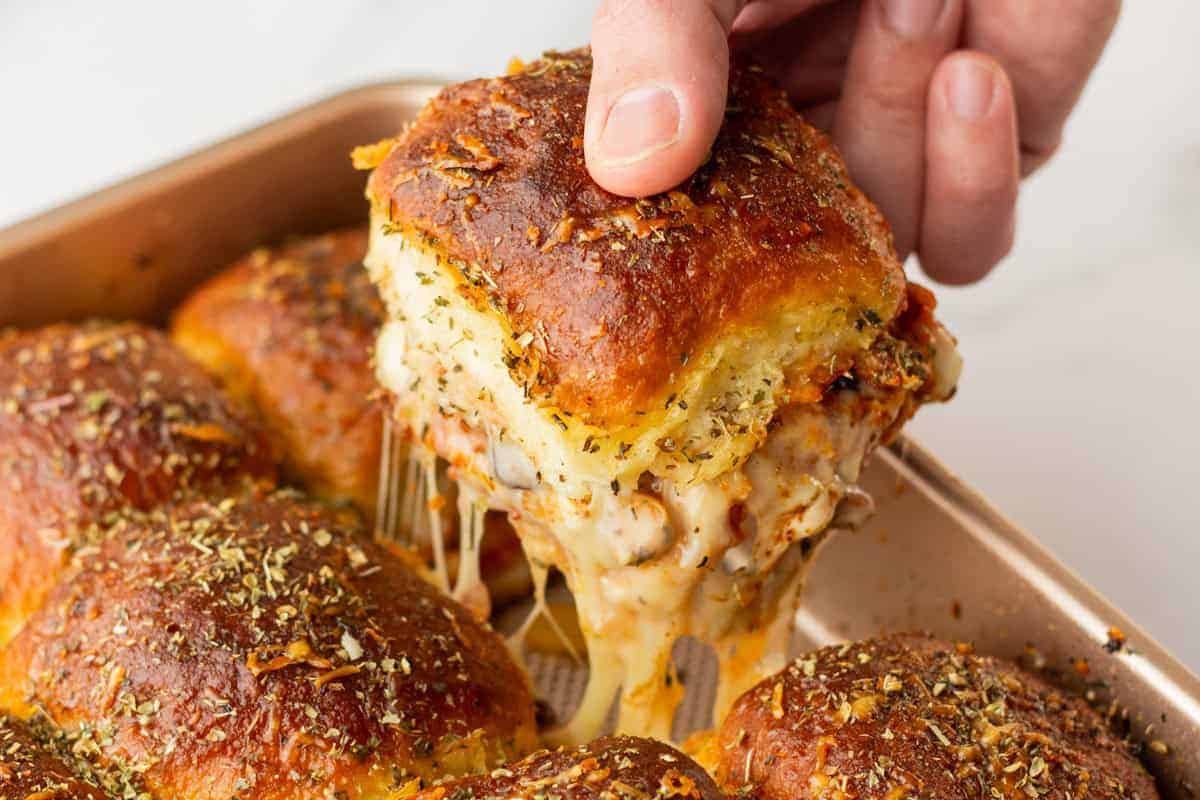 An image of a hand picking up one pizza slider from the baking pan.