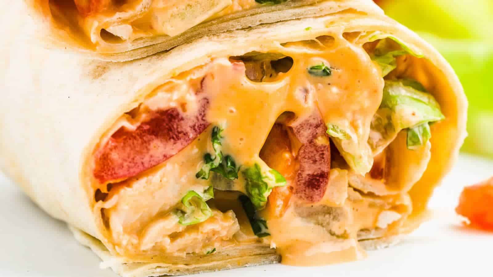 Close-up of a tortilla wrap filled with creamy sauce, lettuce, diced tomatoes, and possibly chicken.