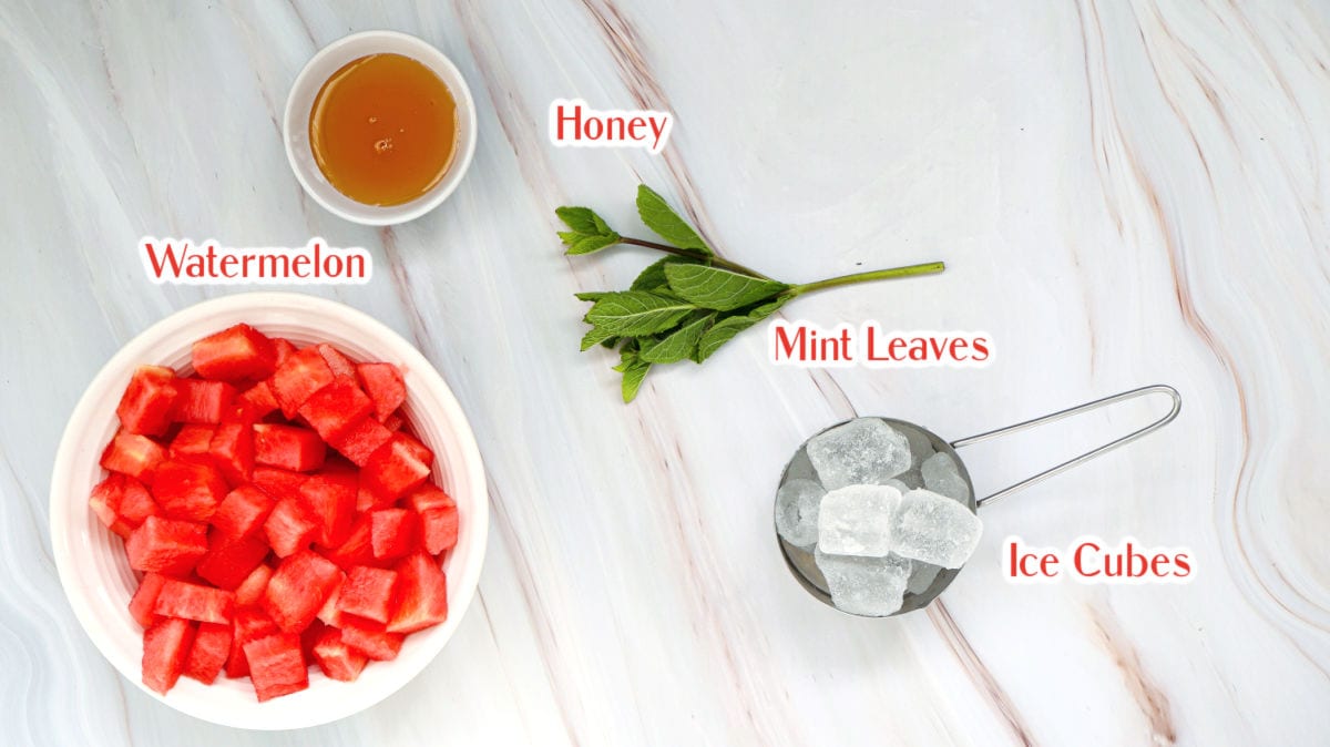 A bowl of cubed watermelon, a small dish of honey, a bunch of mint leaves, and a strainer with ice cubes arranged on a marble surface.