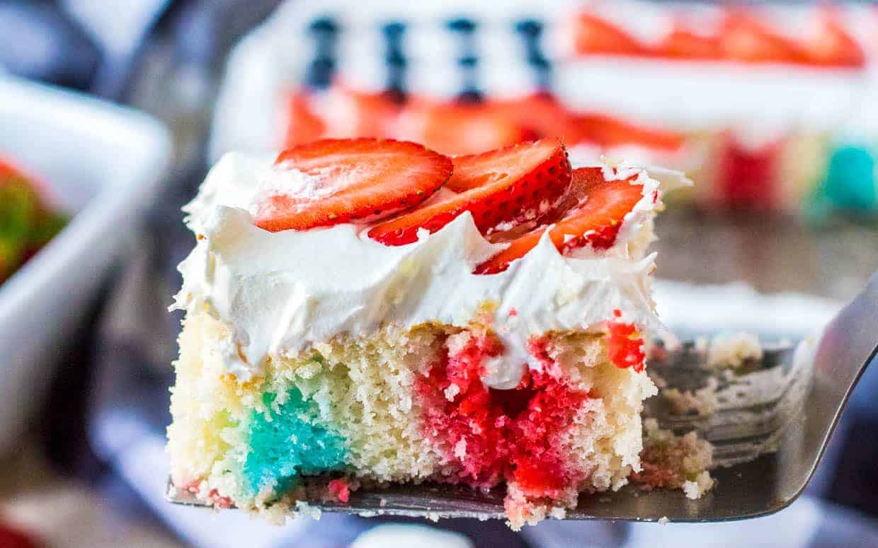 Poke cake with red and blue Koolaid topped with strawberries and blueberries.