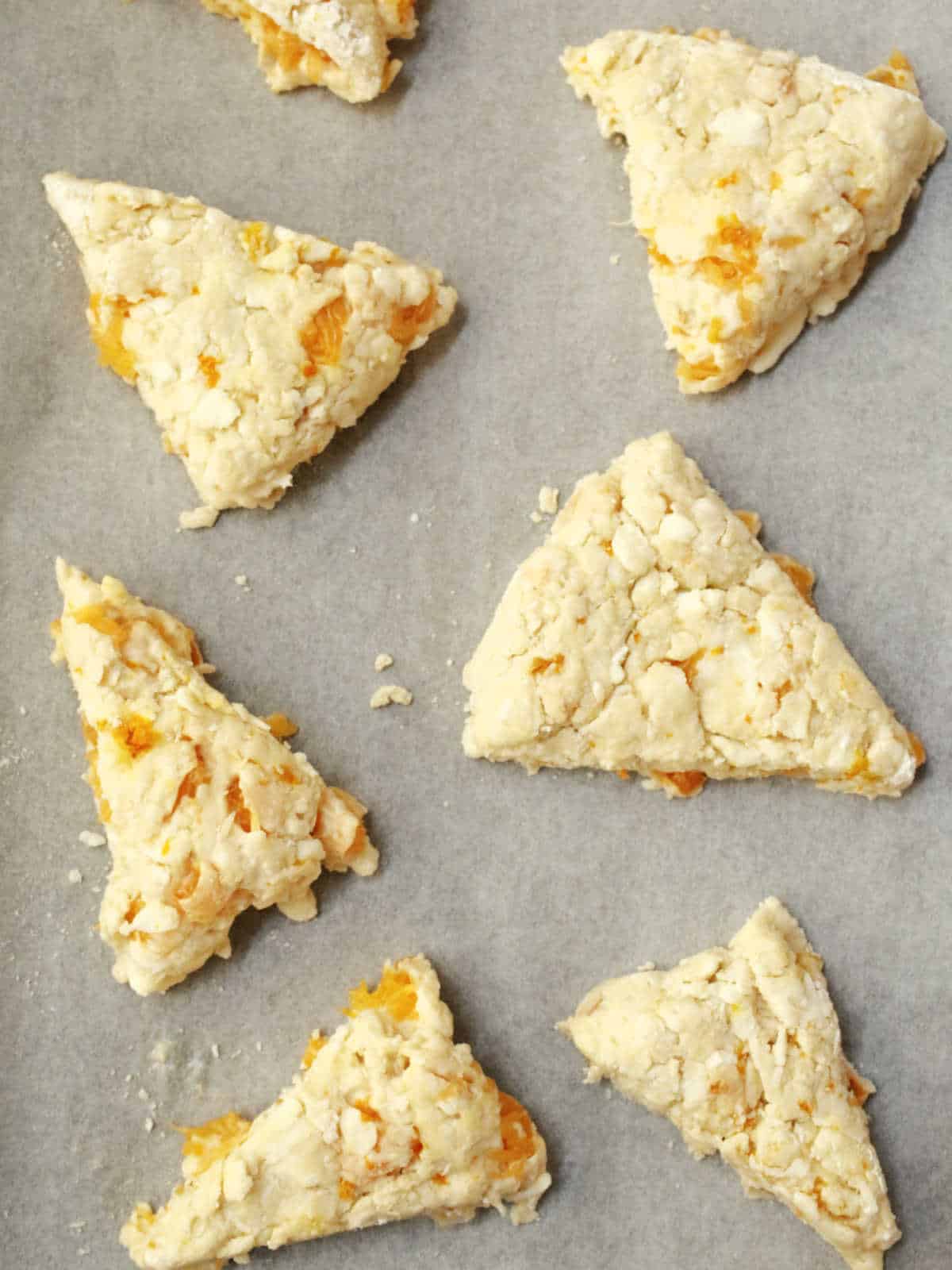 Unbaked scone dough triangles with chunks of fruit on a baking sheet lined with parchment paper.