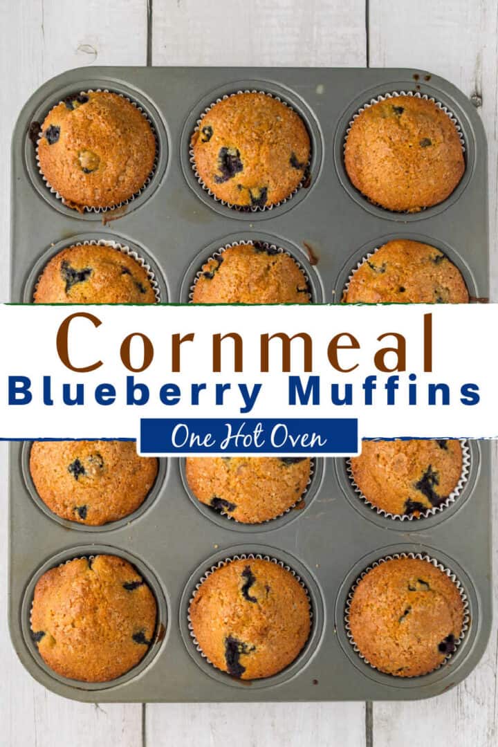 A muffin tin filled with twelve baked cornmeal blueberry muffins, some with visible blueberries on top, placed on a light wooden surface.