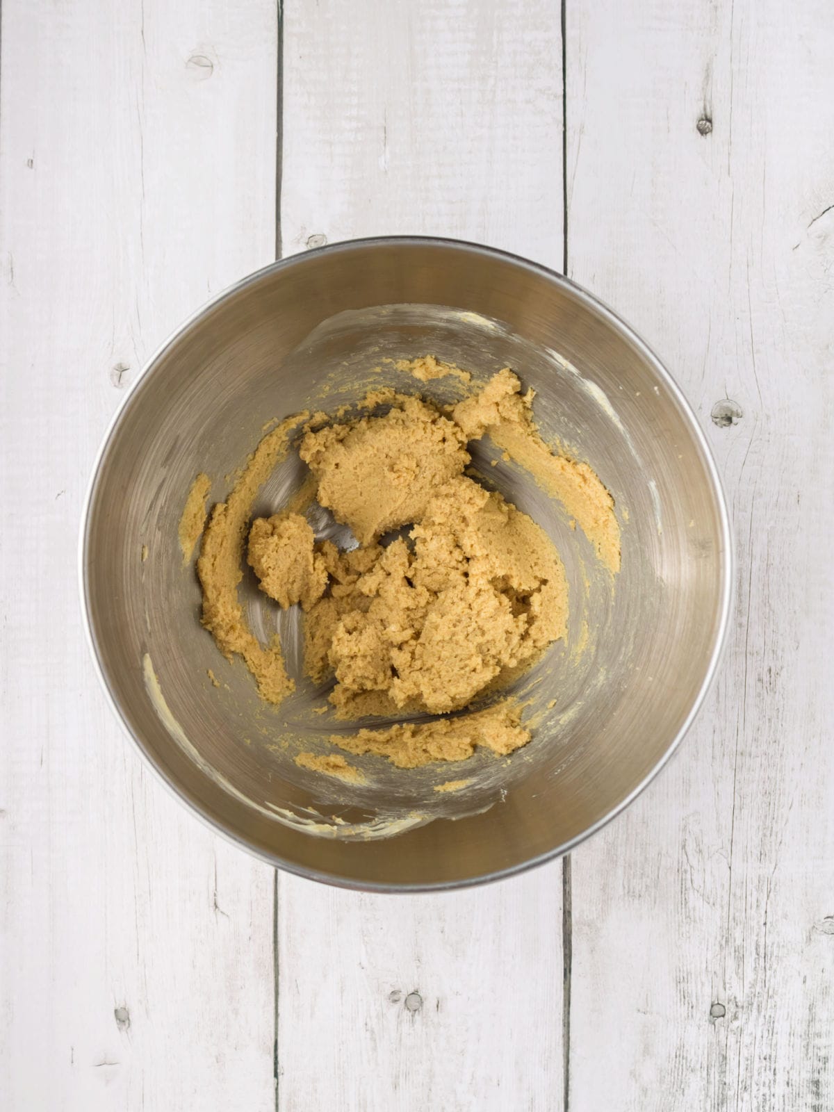 A metal mixing bowl with partially mixed muffin batter sits on a white wooden surface.