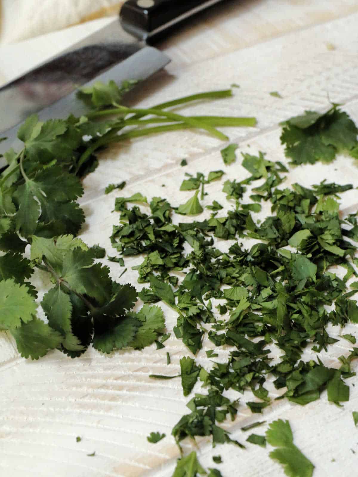 Chopped cilantro and whole cilantro leaves on a cutting board next to a knife.