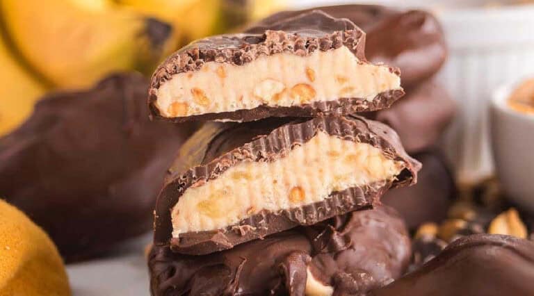 A close-up of chocolate-covered peanut butter banana slices, one cut in half to show the creamy peanut butter and banana filling inside.