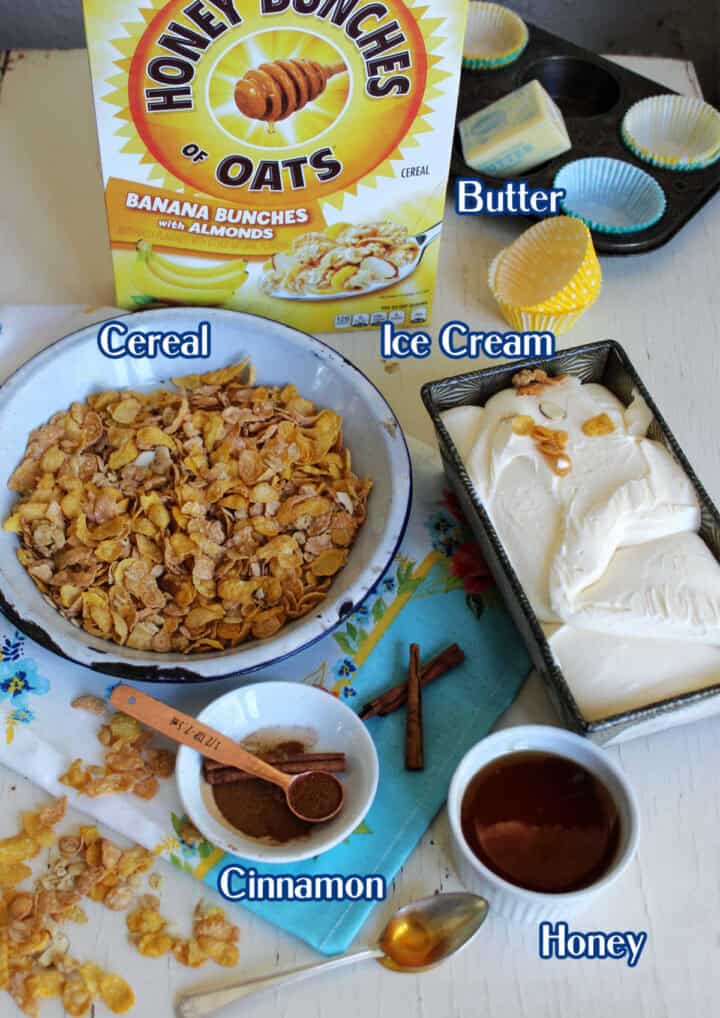 A box of Honey Bunches of Oats, a bowl of cereal, butter, vanilla ice cream, honey, cinnamon, and baking accessories arranged on a white table.