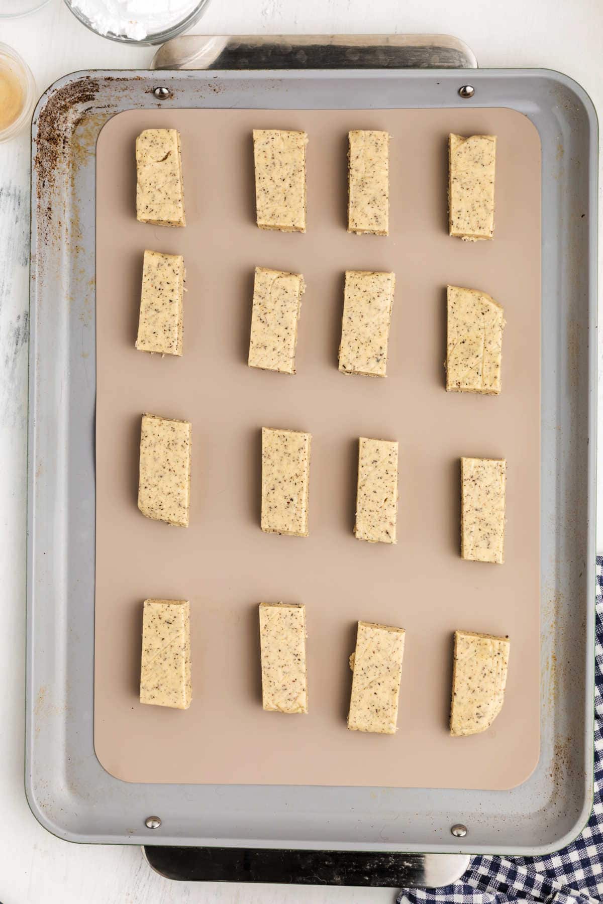 A baking sheet with fifteen rectangular pieces of unbaked chai cookie dough arranged in rows on a parchment-lined tray.