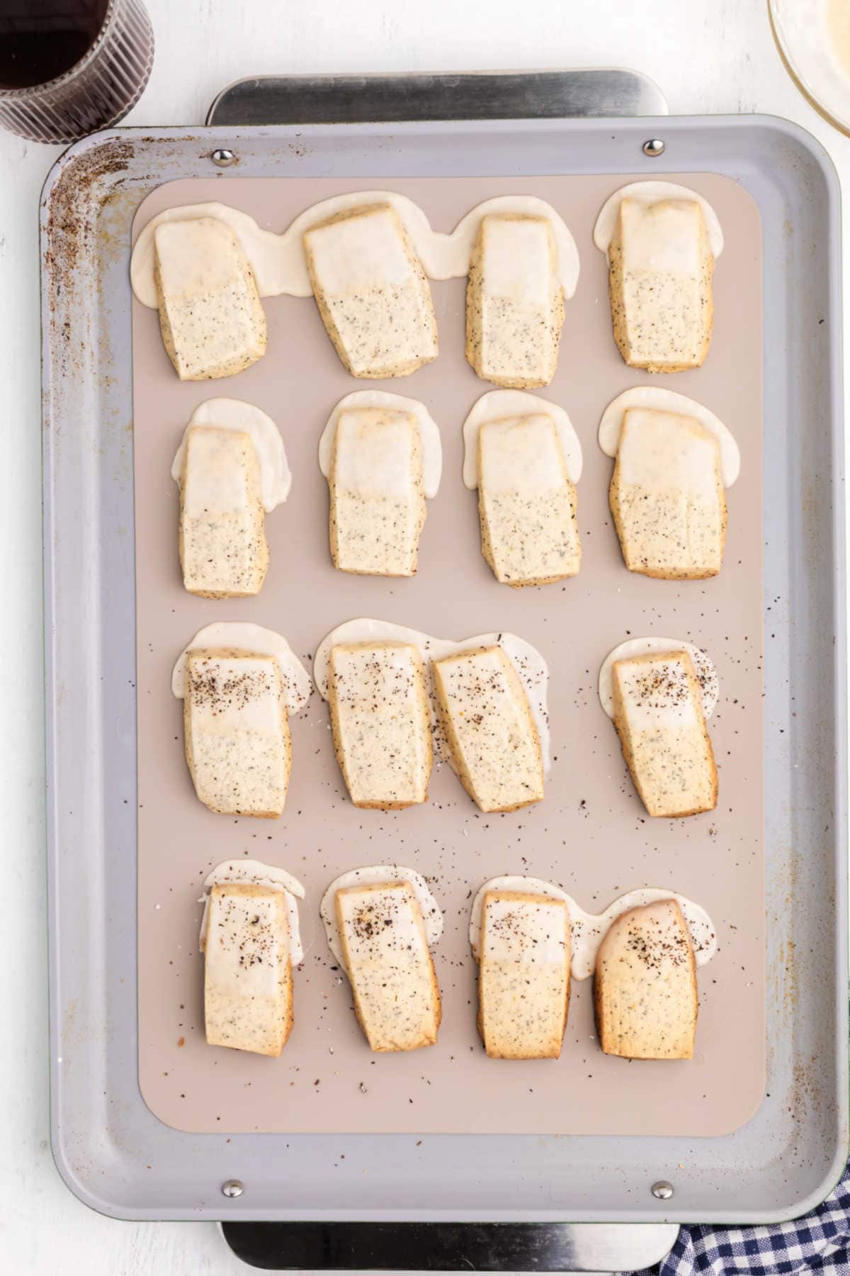 Rectangular shortbread cookies with icing and sprinkled with chai tea are arranged in rows on a baking sheet.