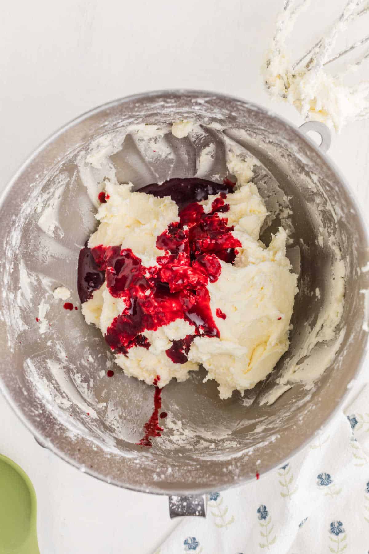 A mixing bowl containing creamed butter and sugar with a splash of red raspberry sauce on top, ready to be mixed together.