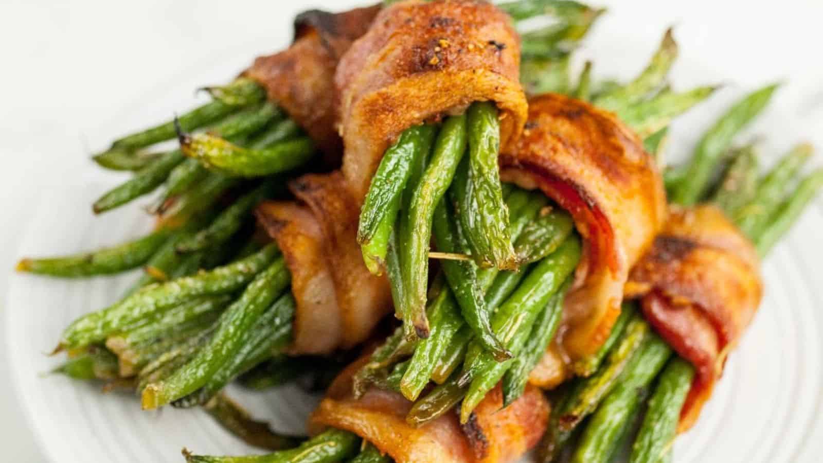 Green beans wrapped in crispy bacon are stacked on a white plate.