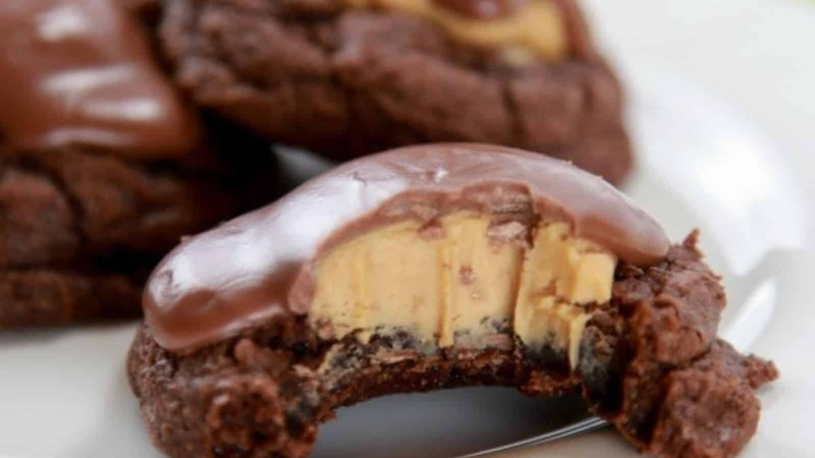 A chocolate cookie with a creamy peanut butter center and chocolate topping, partially eaten, sitting on a white plate.