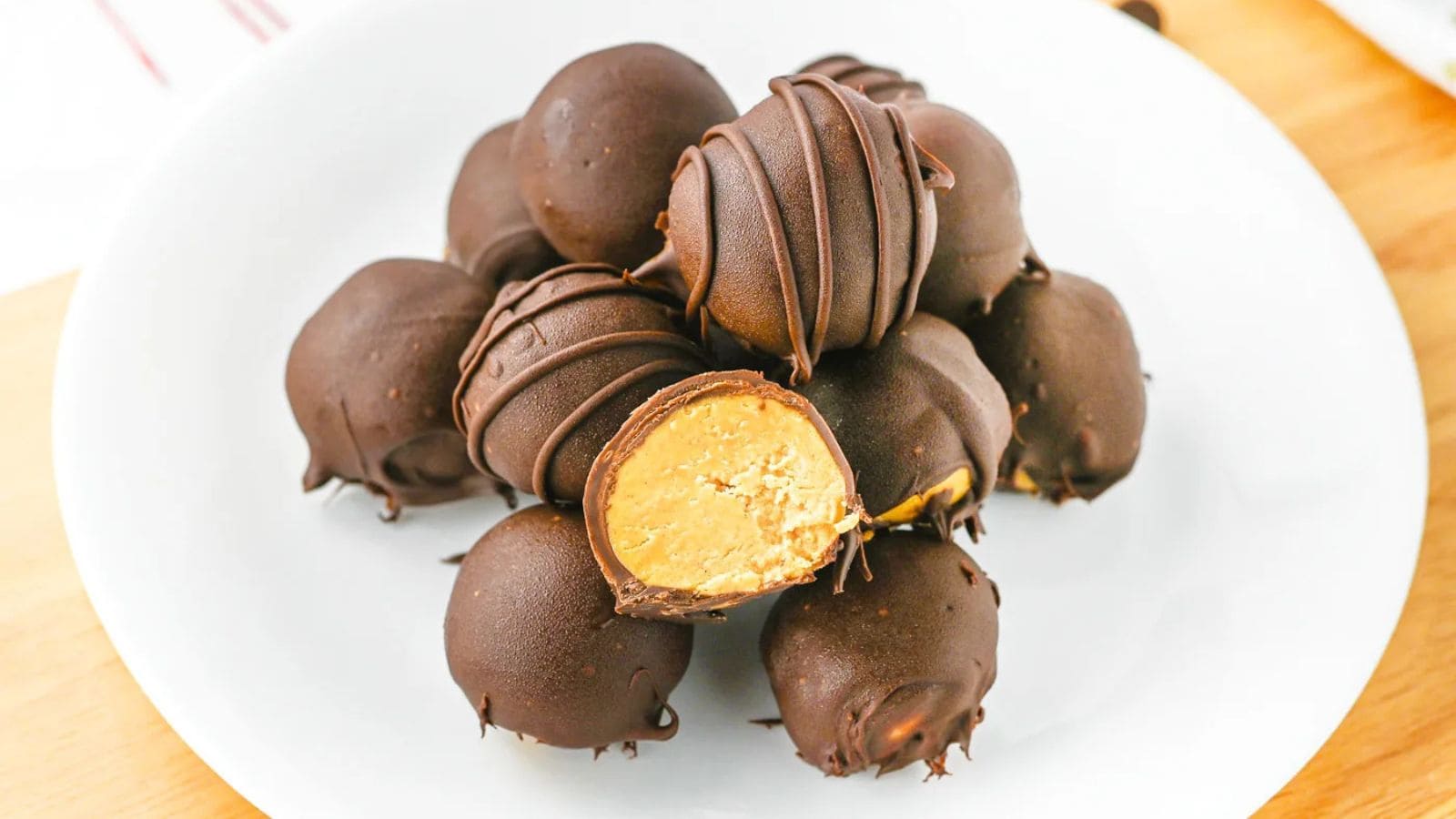 A white plate holds several round chocolate truffles, with one cut open to show a creamy peanut butter filling inside.